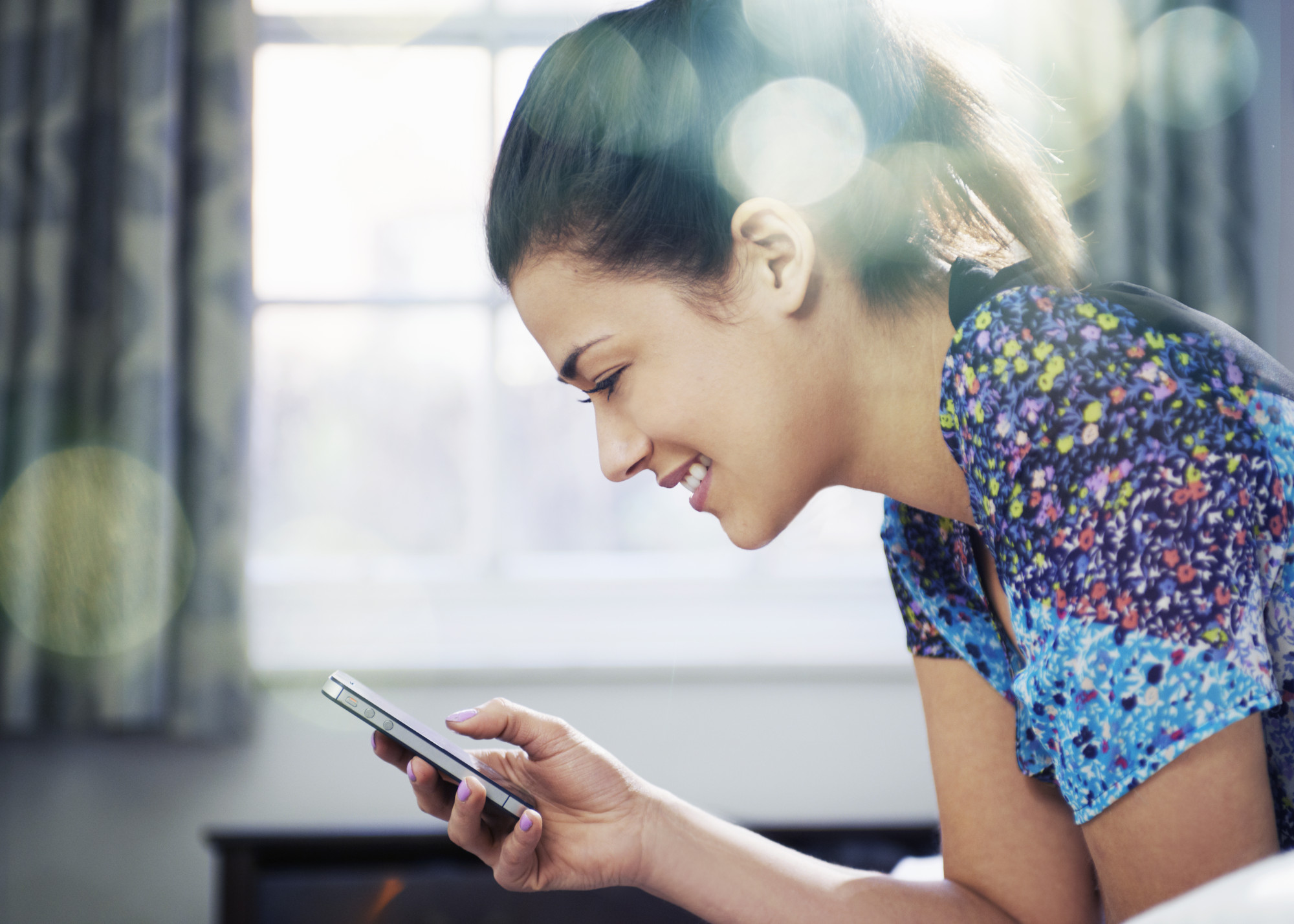 woman on bed smiling and looking at mobile phone